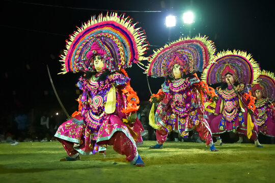 Dynamic Chhau dancers in elaborate masks and colorful costumes, performing acrobatic moves with traditional drums in the background.