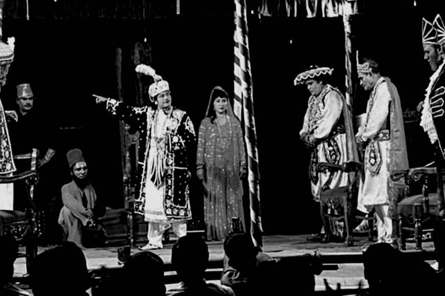Colorful Jatra performance under open-air stage lights with actors in dramatic makeup and elaborate costumes enacting a historical or mythological scene.