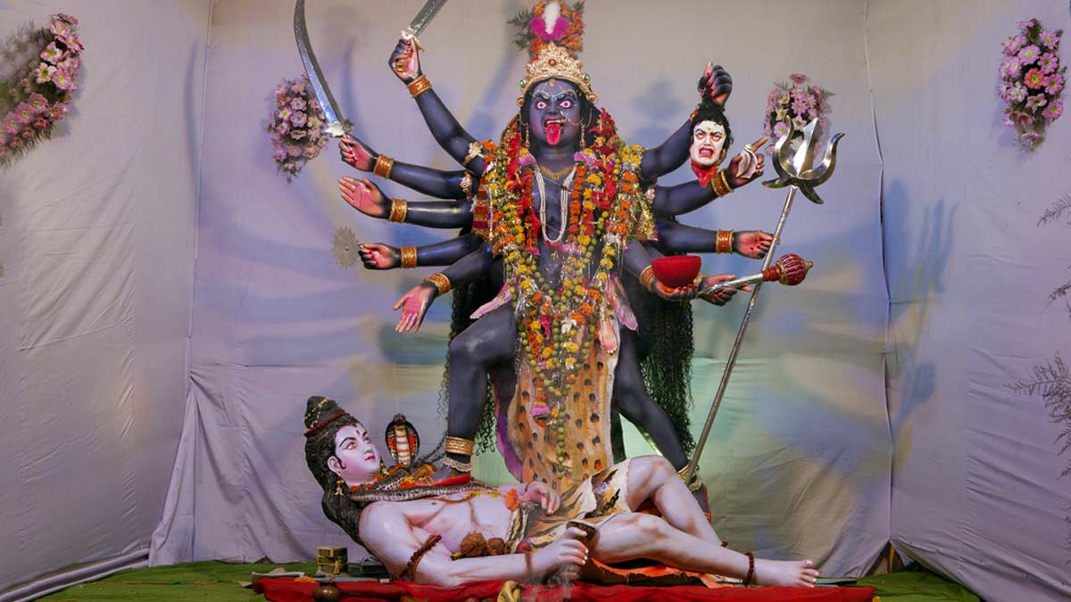 Illuminated Kali Puja pandal with a majestic idol of Goddess Kali, adorned with marigold garlands, as devotees offer prayers during Diwali festivities in Bengal.