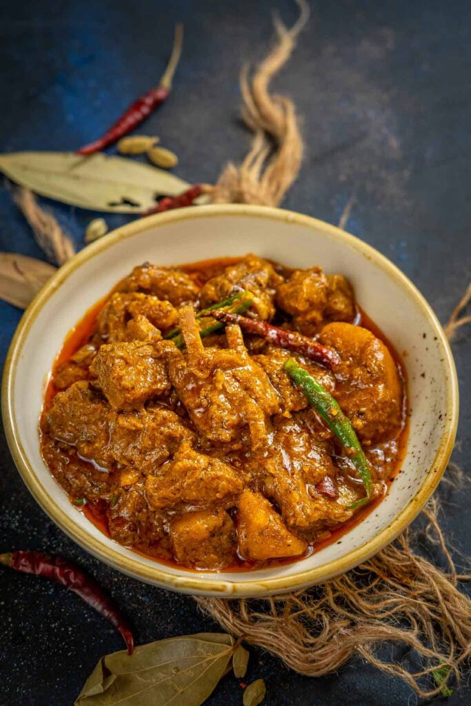 Rich, dark-brown Kosha Mangsho - slow-cooked mutton in thick gravy with caramelized onions and whole spices, served with fluffy luchis.