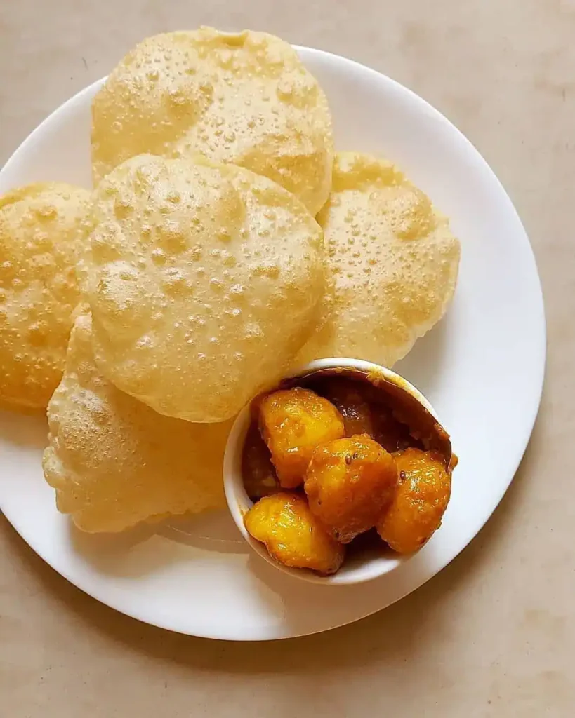 Crispy golden luchis (Bengali puris) paired with spicy alur dom (potato curry) on a traditional bell metal plate