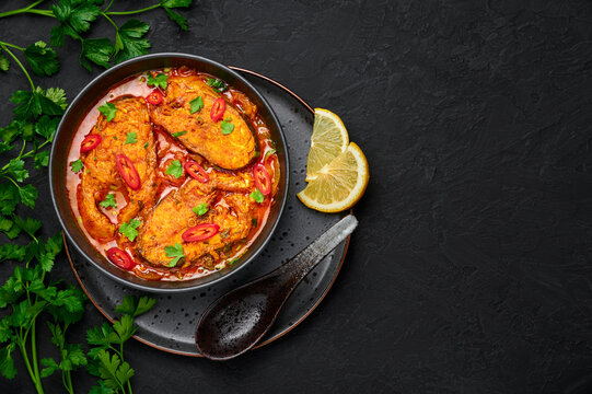 Traditional Bengali Macher Jhol - golden curry with pieces of Rohu fish, potatoes, and aromatic spices, served in a clay bowl with steaming rice.