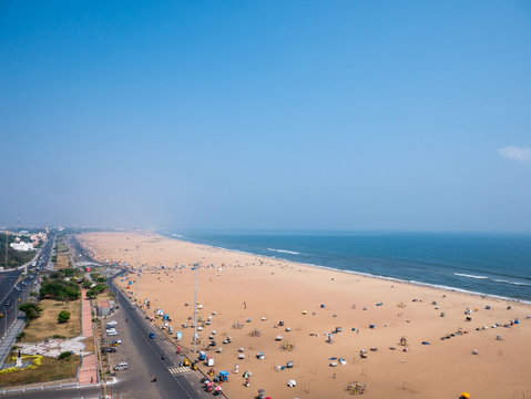 Vibrant Marina Beach in Chennai, with golden sands, bustling crowds, and the iconic Mahatma Gandhi statue against a sunset skyline.