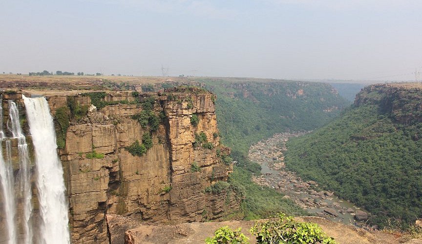 A distant view of a tall, single-stream waterfall dropping from a great height in the Vindhya mountain range.
