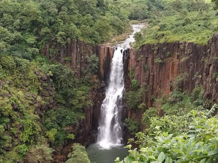 A charming waterfall cascading over moss-covered rocks in a dense forest setting, with visitors enjoying the pool.