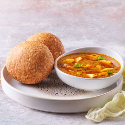 A plate of flaky, golden kachoris served with a bowl of spicy aloo sabzi.