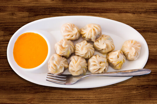 A steaming plate of Tibetan momos served with spicy red chutney.