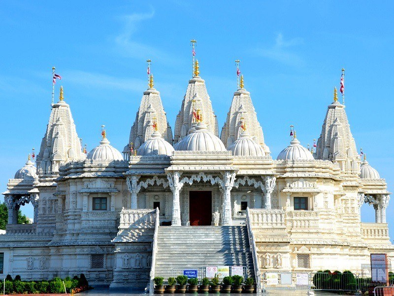 The grand, ornately carved pink sandstone facade of the Shree Swaminarayan Temple in Bhuj, showcasing detailed figures and lattice work.