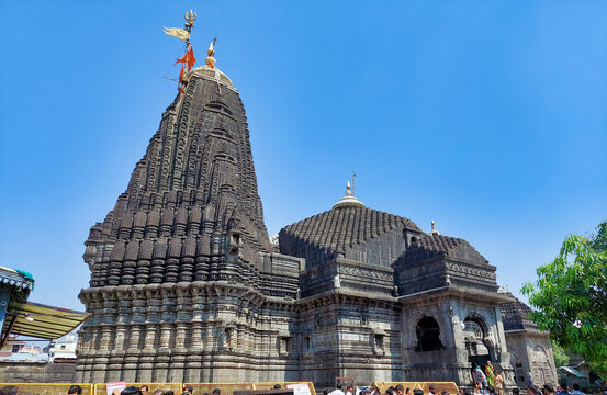 The black stone shikhara (spire) of Trimbakeshwar Temple, adorned with intricate carvings and set against a hill.