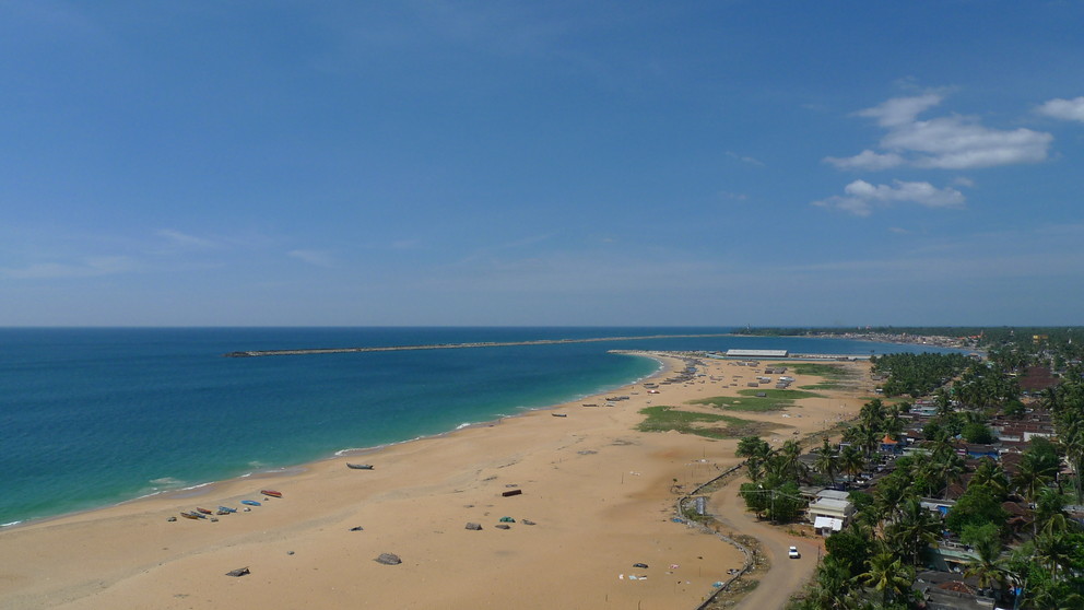 A peaceful shoreline of Kollam Beach with fishing boats on the sand.