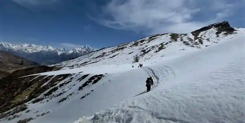 Trekkers on a ridge with Pangarchulla Peak in the background on a clear day.