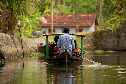 A wooden canoe gliding through narrow village canals in the Kollam backwaters.