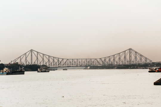 People walking across the pedestrian path of the busy Howrah Bridge with city views.