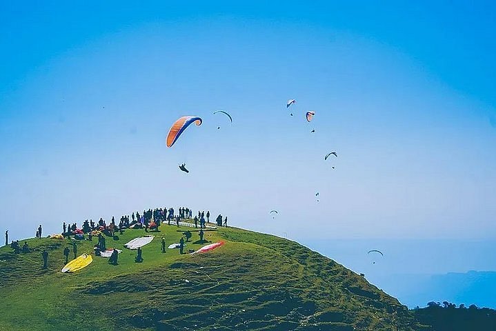 A paraglider soaring above the landscapes of Bir Billing, accessible from Dharamshala.