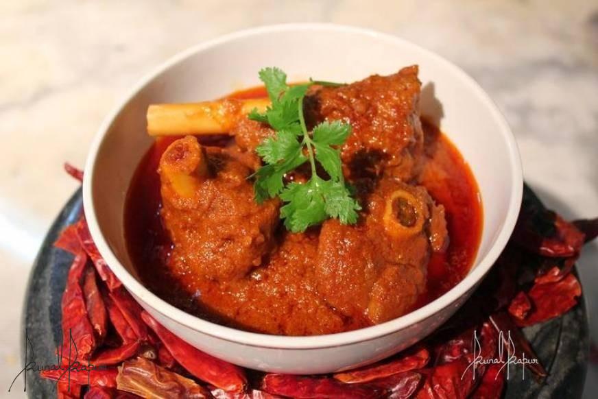 A bowl of vibrant red Laal Maas curry garnished with fresh coriander leaves.