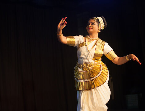 Dancer in white and gold costume performing Mohiniyattam gracefully.