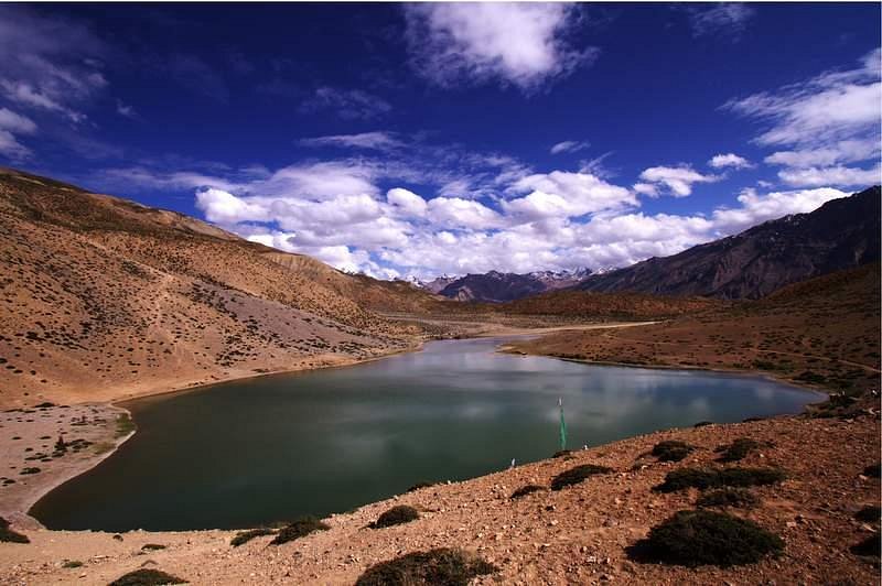 A small, turquoise lake reflecting the rocky cliffs above Dhankar village.