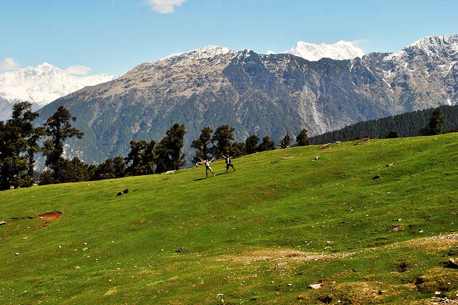 The majestic Garhwal Himalayas rising behind lush green meadows in the Chopta region.