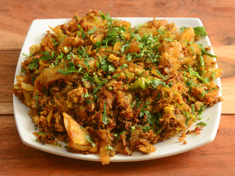 A hot plate of Kothu Parotta being prepared with minced parotta and spices.