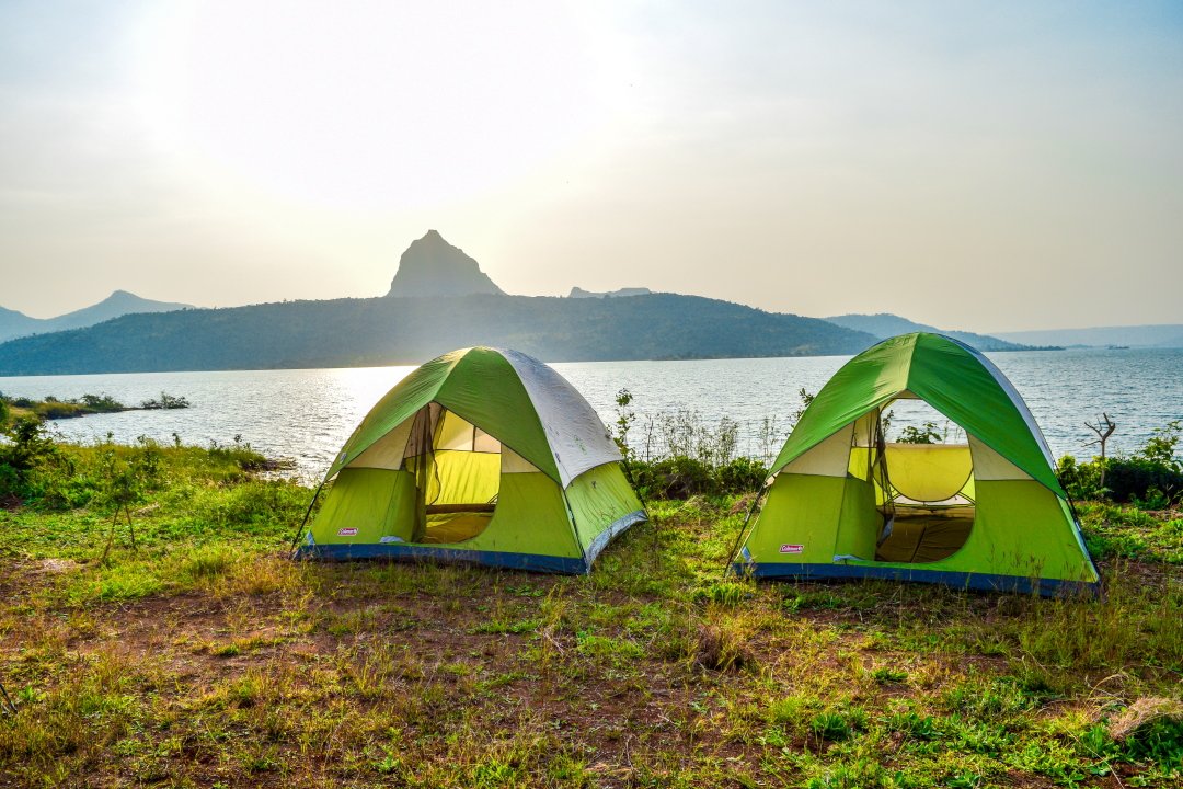 A cozy campsite by a tranquil lakeside, with colorful tents and a campfire under a starry sky near Lonavala.
