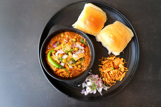 A steaming bowl of spicy misal curry topped with farsan and onions, accompanied by soft pav bread.