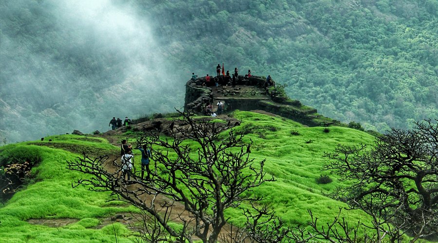 The ancient stone ruins of Rajmachi Fort perched on a lush green hilltop, a historic site overlooking the Lonavala valley.
