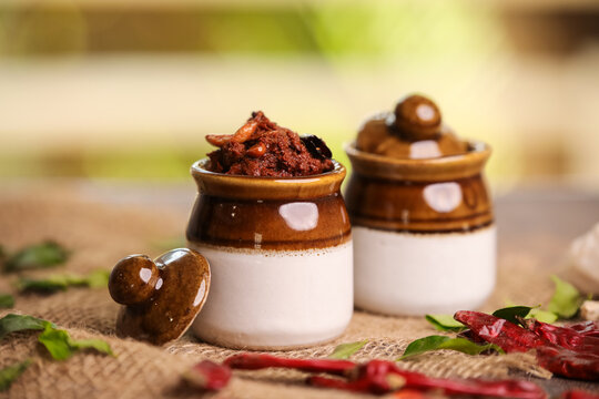 Colorful cones filled with aromatic spice powders and jars of traditional mango pickles arranged on a wooden surface.