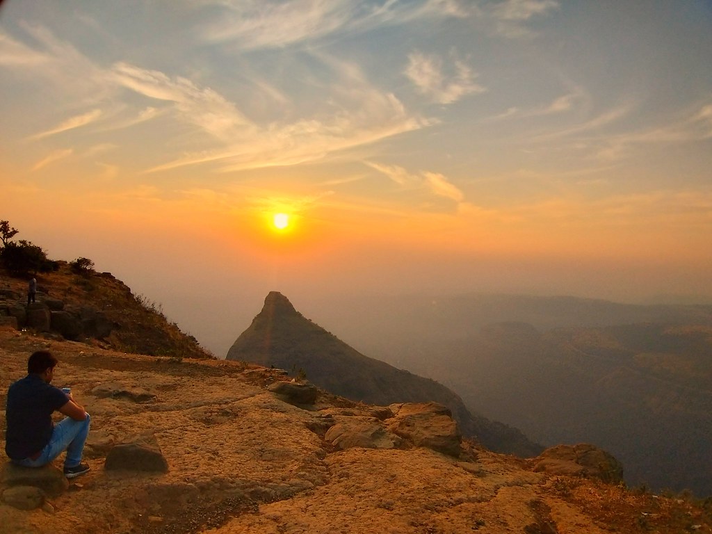 A breathtaking sunset painting the sky in orange and purple hues, viewed from a hilltop overlooking the Lonavala valley.