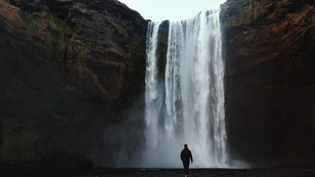A lone hiker walking on a path beside a cascading monsoon waterfall in the lush green hills of Khandala.