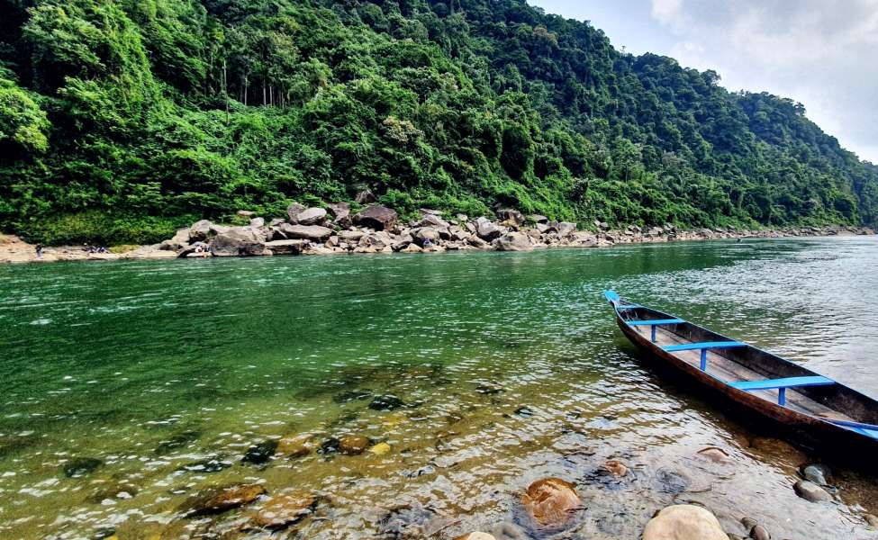 Small grassy sandbar in the middle of Umngot River, accessible by boat, with a single tree and smooth pebbles
