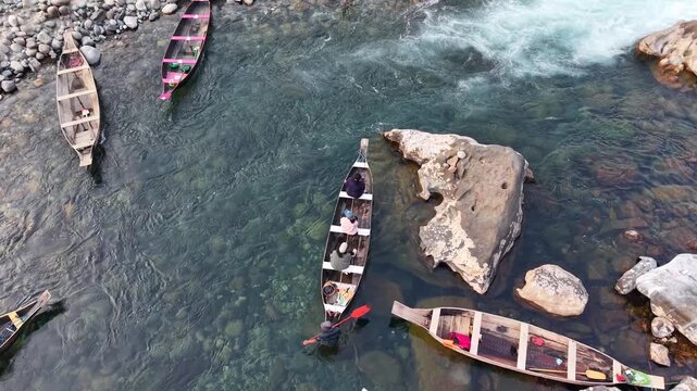 Traditional wooden rowboat carrying two people, floating over submerged boulders visible through the water, Dawki