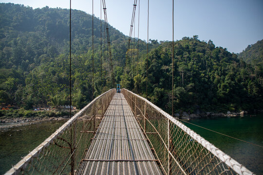Old iron suspension Dawki Bridge spanning the Umngot River, a historic Places to Visit in Dawki, with people walking across and hills behind
