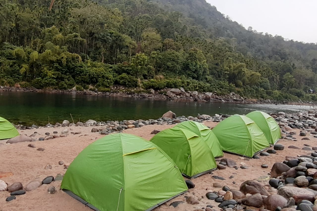 Colorful tents set up on the grassy bank of Umngot River, a favorite Places to Visit in Dawki for overnight camping and bonfires