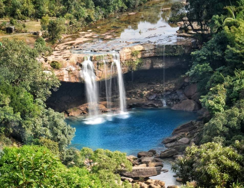 Turquoise waterfall dropping into a shallow pool surrounded by lush forest, a breathtaking Places to Visit in Dawki for picnics and photos
