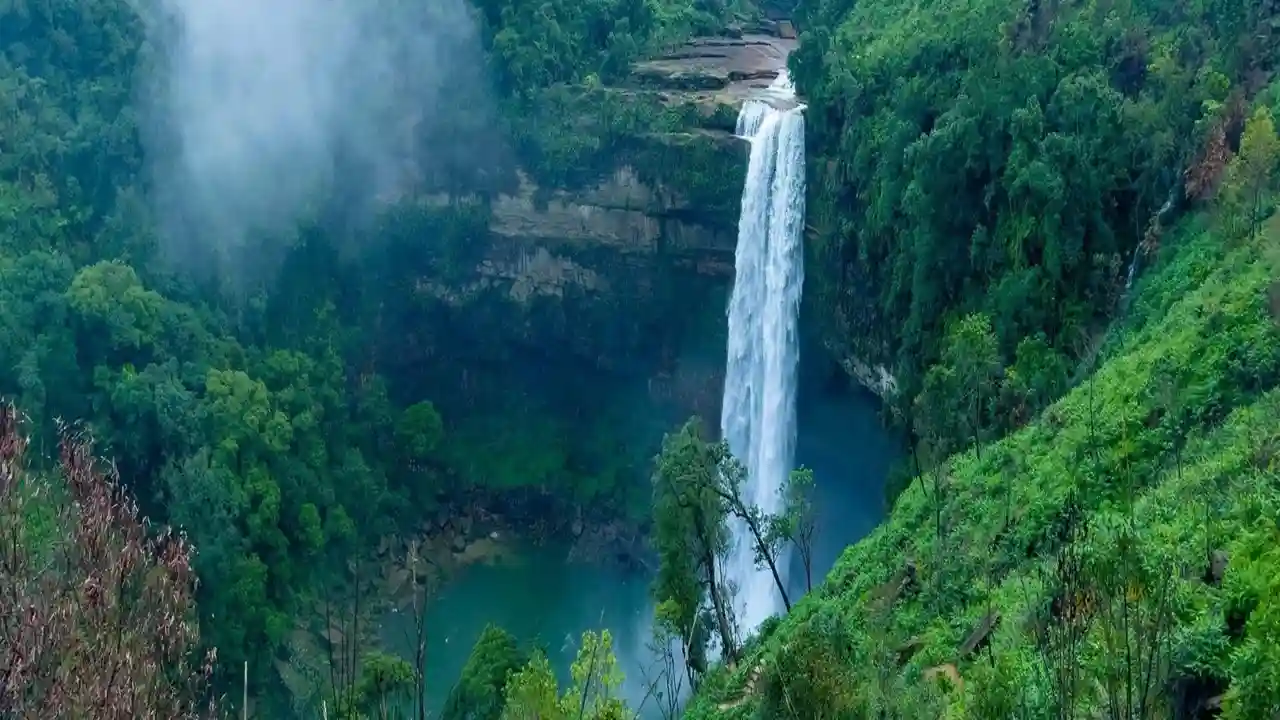 Multi-tiered waterfall cascading into a blue pool surrounded by rocks, a hidden Places to Visit in Dawki for trekking and swimming