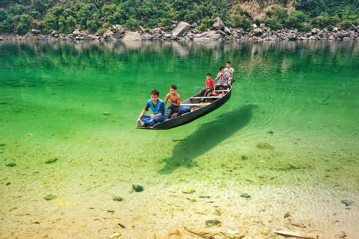Scenic riverside camp at Shnongpdeng with coracle boats tied to the shore and clear water, Dawki