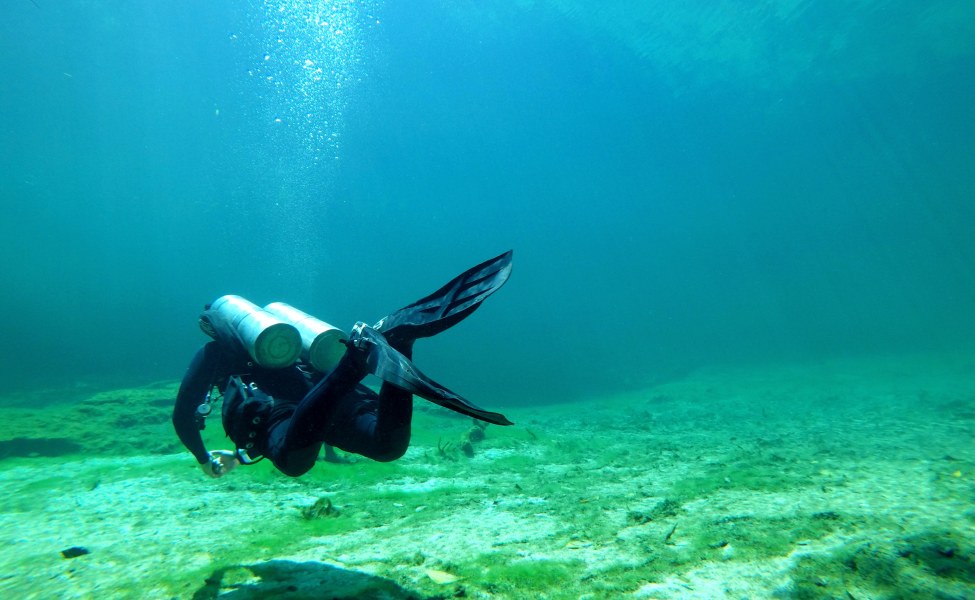 Person snorkeling in Umngot River with flippers and mask, seeing fish over a sandy bottom, Dawki