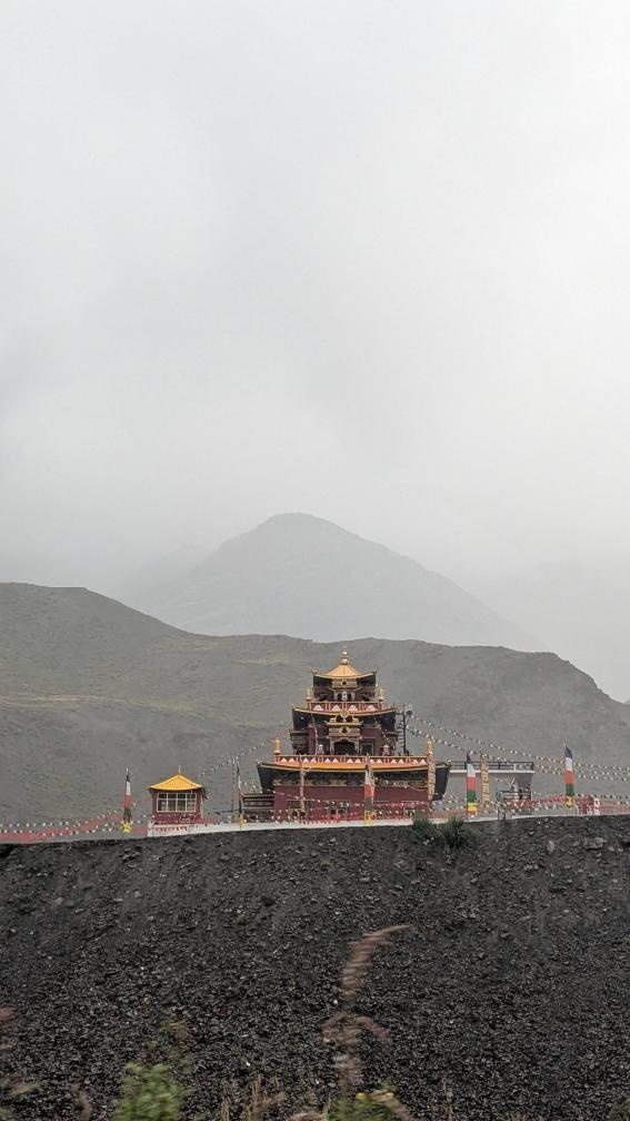 A red and gold Tibetan Buddhist monastery standing in fog against grey misty mountains along the Kinnaur-Spiti road