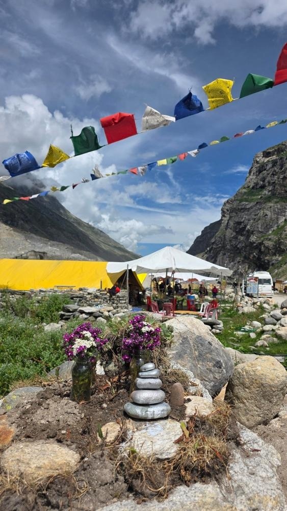 Colorful Buddhist prayer flags and a balanced stone cairn with wildflowers at a campsite near Chandratal Lake, Spiti