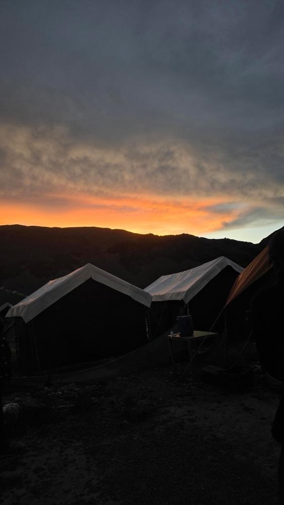 Silhouetted camping tents against a vivid orange and red sunset sky at a high-altitude campsite near Chandratal Lake, Spiti