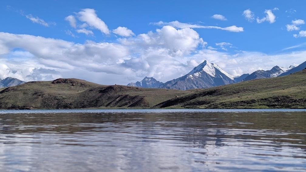 Serene Chandratal Lake with snow-capped Himalayan peaks reflecting on the still blue waters under a bright cloudy sky near Spiti Valley