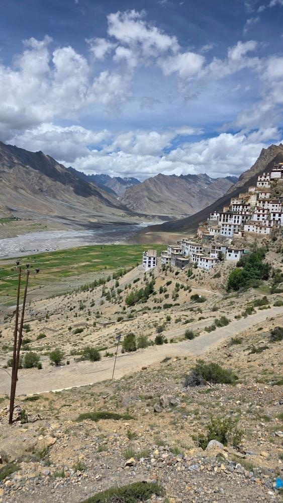 Wide landscape view of Key Monastery nestled on a hillside with the vast Spiti Valley, river plains, and snow-capped peaks stretching into the distance