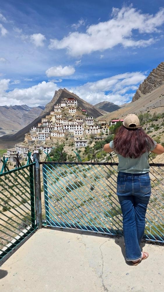 Traveler standing at a viewpoint gazing at Key Monastery perched on a hilltop surrounded by barren Spiti Valley mountains