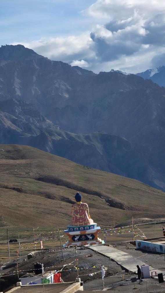 Rear view of the Langza Buddha statue facing vast Spiti Valley mountains and dramatic cloud-covered Himalayan peaks
