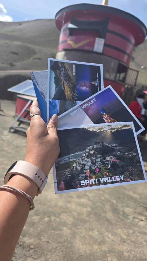 Hand holding Spiti Valley souvenir postcards featuring Key Monastery and starry night sky near Hikkim post office