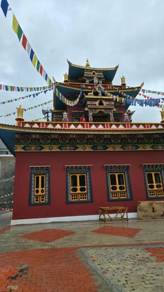 Ornate red and teal Tibetan Buddhist monastery with colorful prayer flags and intricate golden decorations under a cloudy sky in Spiti Valley