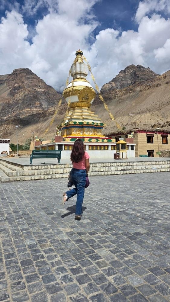 Solo traveler walking toward a large ornate white and golden Buddhist stupa set against the barren brown mountains of Tabo, Spiti Valley