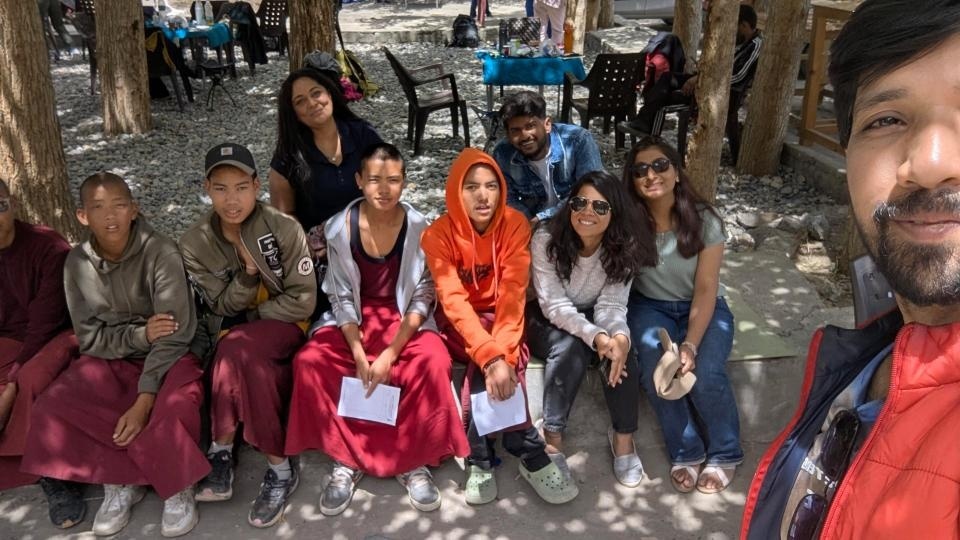 Group of travelers sitting with young Buddhist monks at an outdoor cafe in Spiti Valley